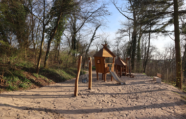 Blick auf ein Kletterhäuschen auf einem Sandplatz unter Bäumen