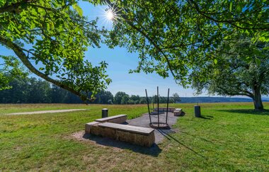 Sonniger Picknickplatz mit Bänken und Feuerstelle auf einer Wiese, umgeben von Bäumen. | © Michael Kühneisen