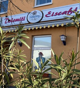 Außenansicht des Eiscafés mit Schild und grünen Pflanzen
