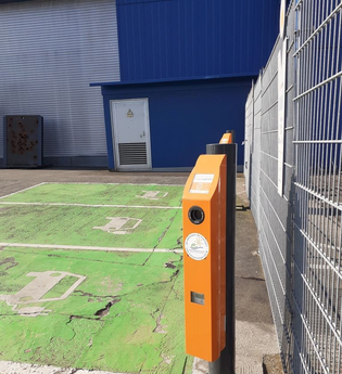 E-Ladesäulen zwischen grüner Parkfläche und Zaun