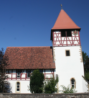 Die Kirche hat einen hohen Turm und rotes Fachwerk | © Touristikgemeinschaft Hohenlohe e. V. | Marion Schlund