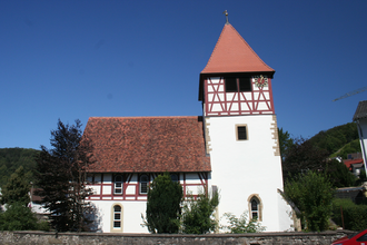 Die Kirche hat einen hohen Turm und rotes Fachwerk | © Touristikgemeinschaft Hohenlohe e. V. | Marion Schlund