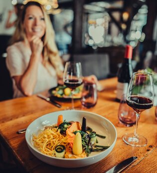 Im Fokus steht ein gedeckter Tisch mit Weingläsern und einem Tellergericht. Der Hintergrund ist unscharf. | © Touristikgemeinschaft HeilbronnerLand