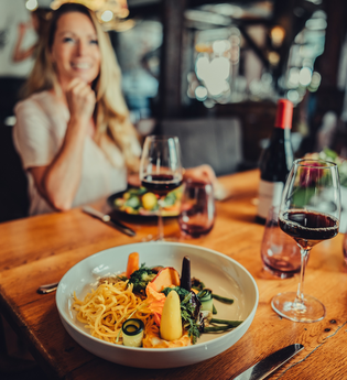 Im Fokus steht ein gedeckter Tisch mit Weingläsern und einem Tellergericht. Der Hintergrund ist unscharf. | © Touristikgemeinschaft HeilbronnerLand