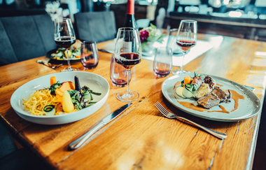 Im Fokus steht ein gedeckter Tisch mit Weingläsern und zwei Tellergerichten. Der Hintergrund ist unscharf. | © Touristikgemeinschaft HeilbronnerLand