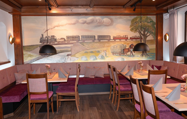 Gaststube mit rot gepolsterten braunen Stühlen und hellen Tischen, an der Wand ein Gemälde mit Dampflokomotive und Wagen in Landschaft | © Gasthof Kocherbähnle GmbH