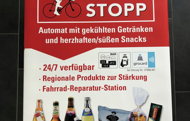 Hier ist ein Poster abgebildet, wo Werbung über den Getränke- und Snackautomaten abgebildet ist.