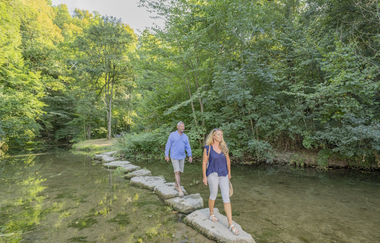 Hammerschmiede umgeben mit grünen Bäumen und zu sehen sind 2 Menschen | © Hohenlohe + Schwäbisch Hall Tourismus e. V.