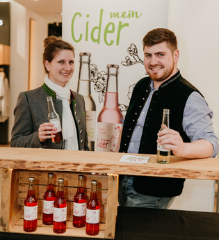 Ein Mann und eine Frau stehen vor einem Roll Up und Regal mit Flaschen | © Touristikgemeinschaft Hohenlohe e. V. | Haußler Hinterespig