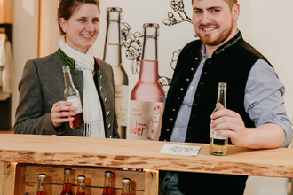 Ein Mann und eine Frau stehen vor einem Roll Up und Regal mit Flaschen | © Touristikgemeinschaft Hohenlohe e. V. | Haußler Hinterespig