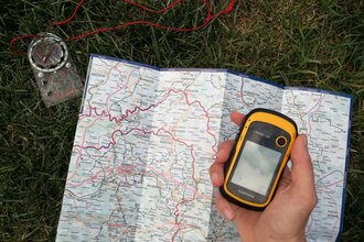 Eine Landkarte und ein Kompass liegen auf dem Boden und das GPS-gerät ist in der Hand | © Touristikgemeinschaft Hohenlohe e.V. | Heffner Outdoor Events