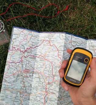Eine Landkarte und ein Kompass liegen auf dem Boden und das GPS-gerät ist in der Hand | © Touristikgemeinschaft Hohenlohe e.V. | Heffner Outdoor Events