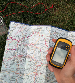 Eine Landkarte und ein Kompass liegen auf dem Boden und das GPS-gerät ist in der Hand | © Touristikgemeinschaft Hohenlohe e.V. | Heffner Outdoor Events