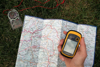 Eine Landkarte und ein Kompass liegen auf dem Boden und das GPS-gerät ist in der Hand | © Touristikgemeinschaft Hohenlohe e.V. | Heffner Outdoor Events