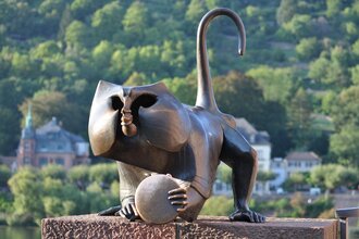 Bronzene Statue in Affenform, die auf einer Steinmauer positioniert ist. Der Affe hält einen Spiegel in der Greifhand. | © Heidelberg Marketing GmbH