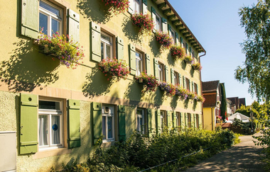 Ein gelbes Haus mit grünen Fensterläden und Blumenkästen in einer sonnigen Straße. | © Stuttgart-Marketing GmbH, Sarah Schmid