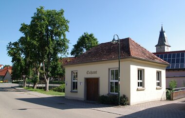 Das Gebäude des historischen Eichamts Blaufelden mit Bäumen und dem Kirchturm im Hintergrund | © Hohenlohe + Schwäbisch Hall Tourismus e. V.