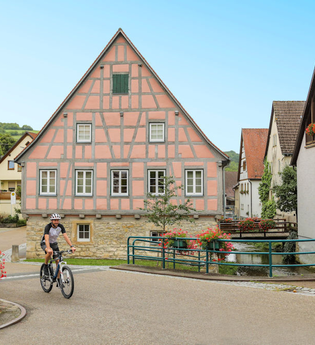 Ein Radfahrer fährt vor dem historischen Fachwerk-Rathaus | © Touristikgemeinschaft Hohenlohe e. V. |  Andi Schmid
