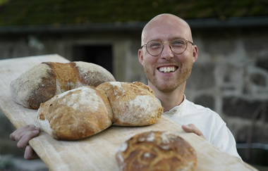 Ein Mann hält frische Brotlaibe auf einem Holzbrett hoch | © Touristikgemeinschaft Hohenlohe e. V. | Hofgut Hermersberg