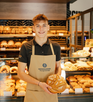 Ein Verkäufer in der Bäckerei hält ein Brot in der Hand | © Touristikgemeinschaft Hohenlohe e. V. | Marc Bauer