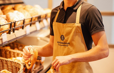 Ein Verkäufer packt frische Brezeln in einer Backwarentüte | © Touristikgemeinschaft Hohenlohe e. V.  | Marc Bauer