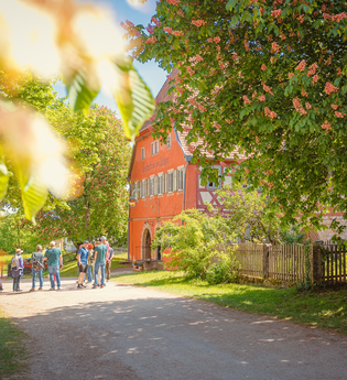 Gruppe von Menschen vor einem historischen Gebäude in Wackershofen, umgeben von blühenden Bäumen. | © © Stadt Schwäbisch Hall - Michael Kühneisen