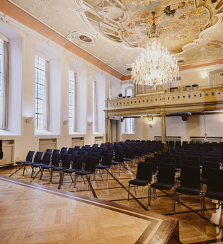 Innenansicht eines Festsaals mit Stühlen, einem Flügel und einem Kronleuchter. | © NICO KURTH