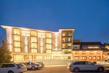 Das Hotel ist nachts hell beleuchtet, davor ist ein Parkplatz für Pkw | © Touristikgemeinschaft Hohenlohe e. V.