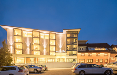 Das Hotel ist nachts hell beleuchtet, davor ist ein Parkplatz für Pkw | © Touristikgemeinschaft Hohenlohe e. V.