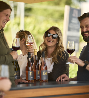 Fröhliche Weinrunde an einem Probierstand im Weinberg mit mehreren Personen, die anstoßen und lachen. | © Tourimia Tourismus GmbH | Stefan Leitner Photography