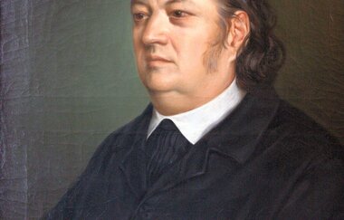 Porträt von Justinus Kerner, gemalt von Ottavio d’Albuzzi, zeigt einen Mann in dunkler Kleidung mit einem Wappen im Hintergrund. | © Originalgemälde im Besitz des Justinus-Kerner-Vereins e.V.