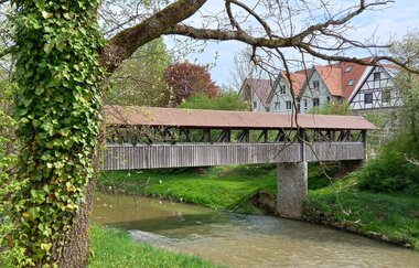 Holzbrücke über einen Fluss in Gaildorf, umgeben von Bäumen und Fachwerkhäusern. | © Petra Natzkowski