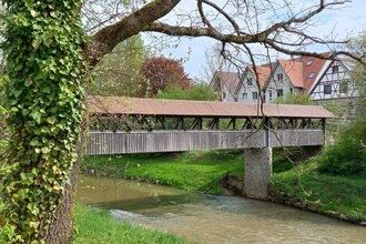 Holzbrücke über einen Fluss in Gaildorf, umgeben von Bäumen und Fachwerkhäusern. | © Petra Natzkowski