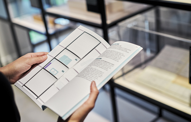 Eine Person hält eine Broschüre in den Händen, dahinter sind Regale mit Ausstellungsstücken | © Touristikgemeinschaft Hohenlohe e. V. | Kocherwerk Haus der Verbindungstechnik