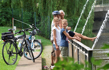 Zwei Jugendliche und ein Mann und Frau stehen an einer Wasserfontäne | © Touristikgemeinschaft Hohenlohe e. V. | Susanne Schleussner