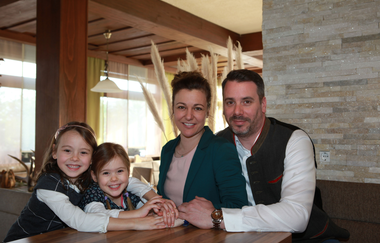 Die Eltern und zwei Mädchen sitzen zusammen am Tisch und lächeln in die Kamera | © Touristikgemeinschaft Hohenlohe e. V. | Landhotel Küffner