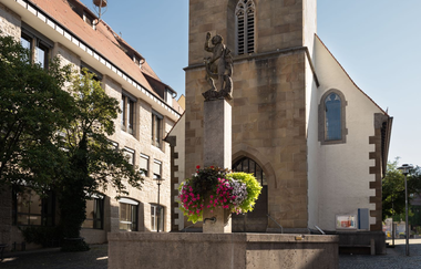 Zu sehen ist ein Brunnen vor einer Kapelle mit einer Statue und Blumen | © Stadverwaltung Crailsheim