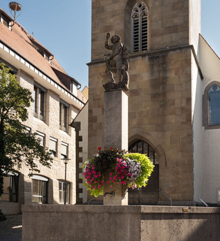 Zu sehen ist ein Brunnen vor einer Kapelle mit einer Statue und Blumen | © Stadverwaltung Crailsheim