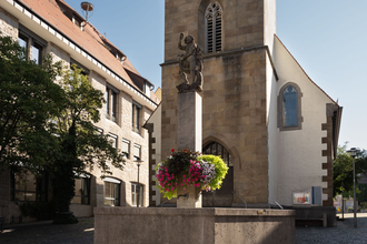 Zu sehen ist ein Brunnen vor einer Kapelle mit einer Statue und Blumen | © Stadverwaltung Crailsheim