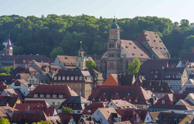 Blick auf die Kirche St. Michael in Schwäbisch Hall mit umliegenden Gebäuden und Wald im Hintergrund. | © Michael Kühneisen