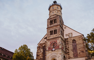 Michaelskirche in Schwäbisch Hall mit Turm und Uhr vor bewölktem Himmel. | © Nico Kurth
