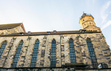 Seitenansicht der Michaelskirche in Schwäbisch Hall mit gotischen Fenstern und einem Turm vor blauem Himmel. | © Stuttgart-Marketing GmbH, Sarah Schmid