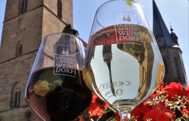 Zwei Gläser mit dem Logo Hohenloher Weindorf stehen auf einem Brunnen vor der Stiftskirche | © Touristikgemeinschaft Hohenlohe e. V. | Jürgen Koch