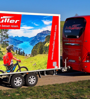 Ein roter Bus zieht einen Fahrradanhänger. | © Müller Reisen Massenbachhausen