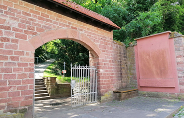 Ziegelsteinwand mit integriertem Torbogen, geöffnetem schmiedeiserenem Tor und einer Gedenktafel an der Seite. | © Stadt Weinheim - Jasmin Wolf
