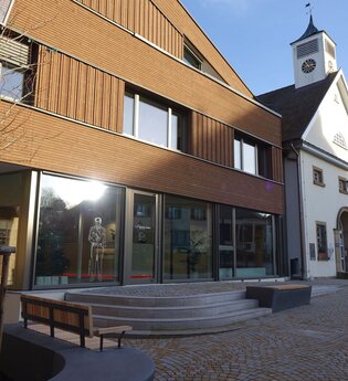 Außenansicht der Tourist-Info mit Glasfront und moderner Holzfassade. Vor den Gebäude stehen Bänke zum Verweilen. | © Neckar-Zaber-Tourismus e.V.