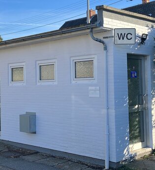 Kleines weißes Gebäude mit WC Schild