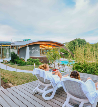 Zwei Frauen liegen auf Liegestühlen und unterhalten sich, im Hintergrund sieht man das parc vital Gebäude sowie ein Schwimmbecken | © Stadtwerke Crailsheim