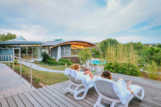 Zwei Frauen liegen auf Liegestühlen und unterhalten sich, im Hintergrund sieht man das parc vital Gebäude sowie ein Schwimmbecken | © Stadtwerke Crailsheim