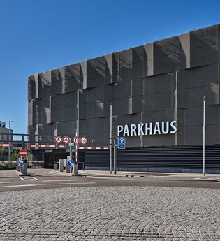 Seitenansicht auf die Fassade eines modernen Parkhauses mit Schriftzug Parkhaus und Schranken